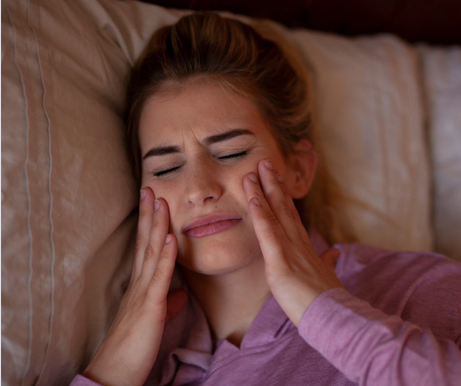 A woman asleep, holding her face in bed, experiencing tooth pain during the night.